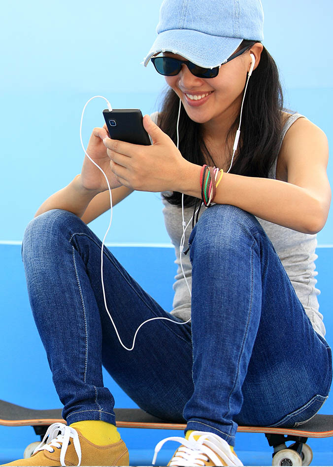 woman sitting on skateboard with earbuds in typing on her phone