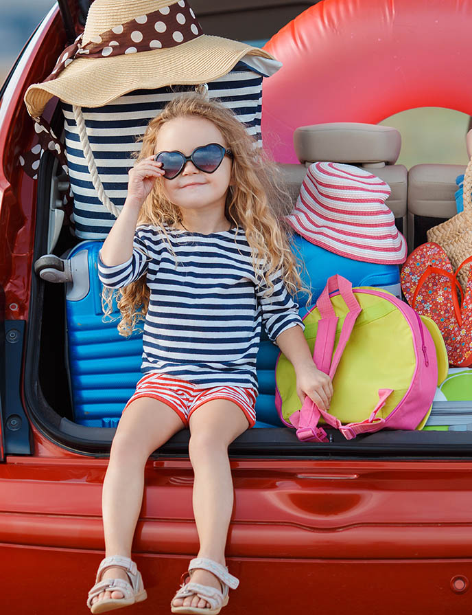 child with sunglasses on sitting on the tailgate of a vehicle