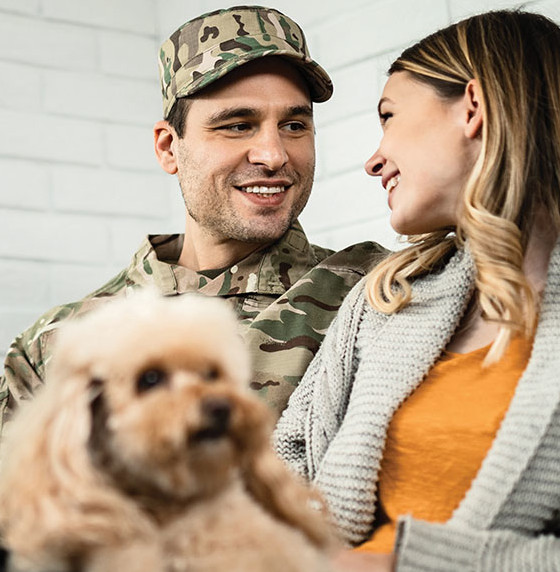 man in military uniform smiling at woman holding a dog