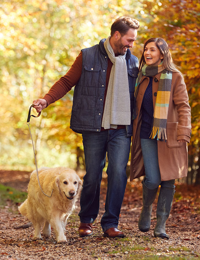 image of man and woman walking dog in fall leaves