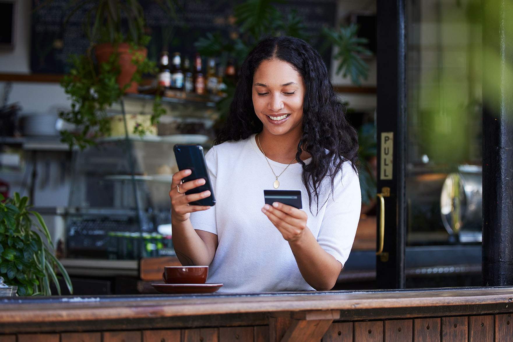 Woman smiling as she holds credit card and enters something onto her mobile phone.