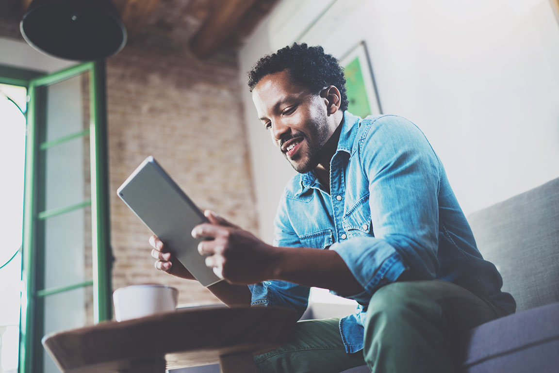 Bearded smiling African man using tablet while on sofa